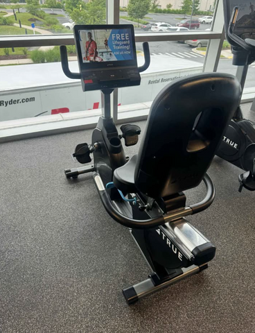 Front view of a True Fitness R900 commercial recumbent exercise bike featuring the Unite 2.0 touchscreen console interface.